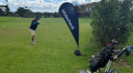 A golfer ready a swing in front of a Molecheck teardrop flag