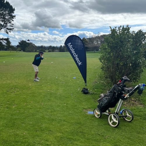 A golfer ready a swing in front of a Molecheck teardrop flag