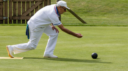 An elderly man mid throwof a bowls ball