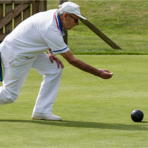 An elderly man mid throwof a bowls ball